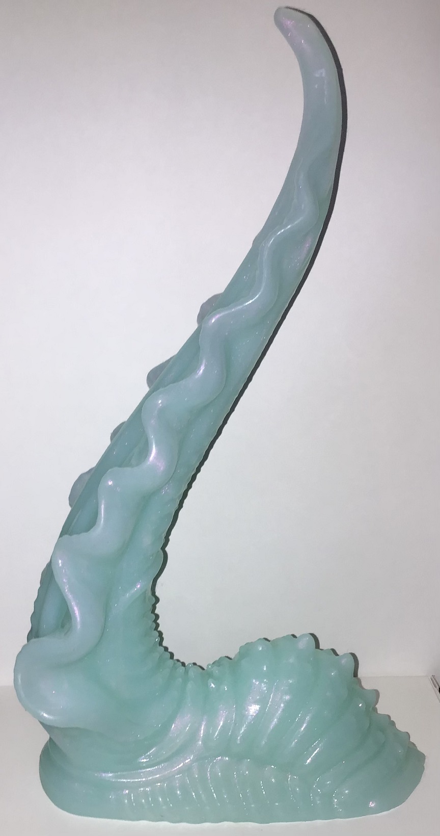 Side profile of a tentacle that's thick at the bottom and tapers to a very thin tip. Wavy fins line either side. The base is a hump with bumpy texture. It's jade green with pink shimmer.