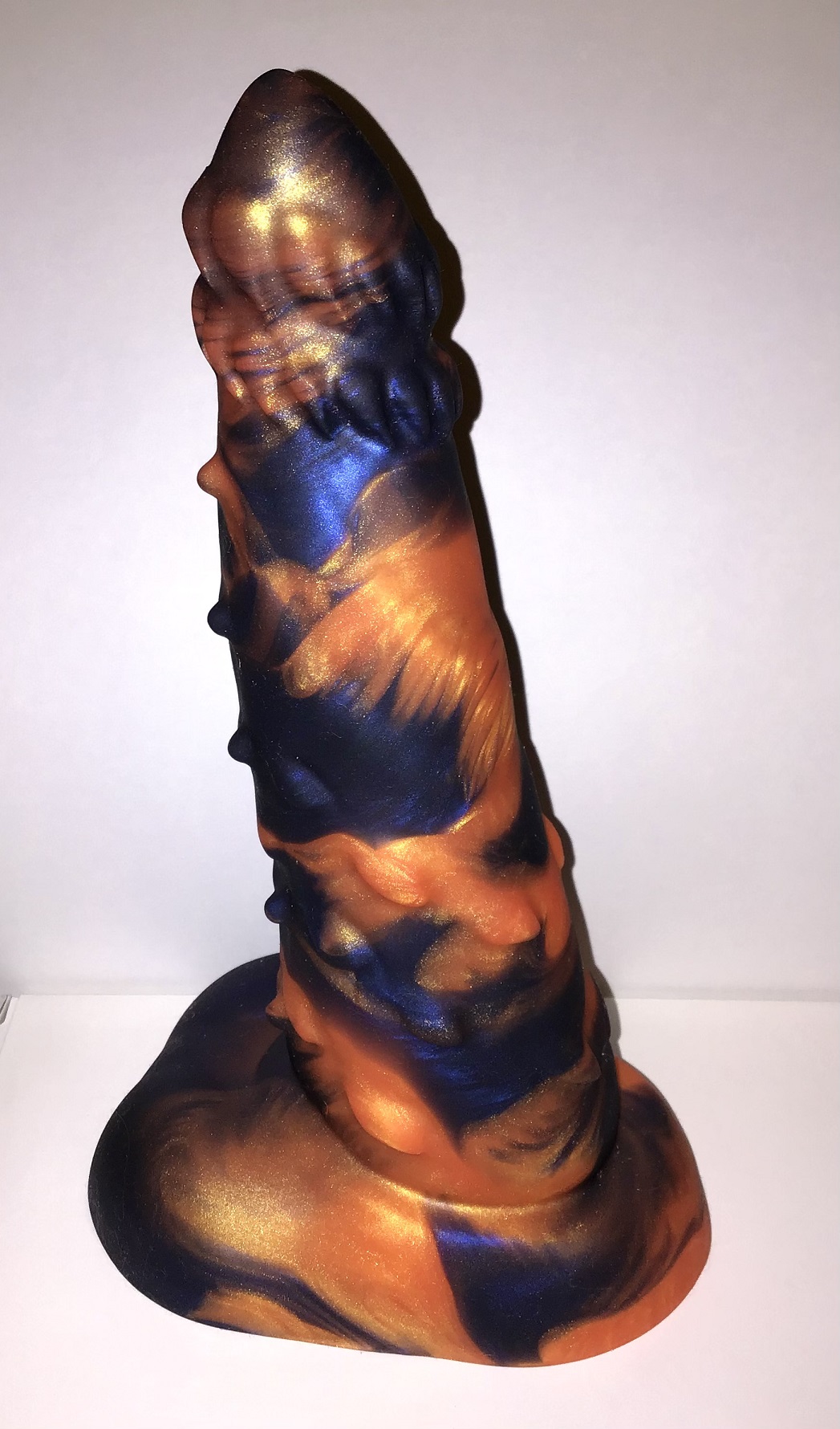 A feline model that tapers to a barbed head, with piercings and points along the shaft and balls at the base. It's a marble of shimmering orange and midnight blue.